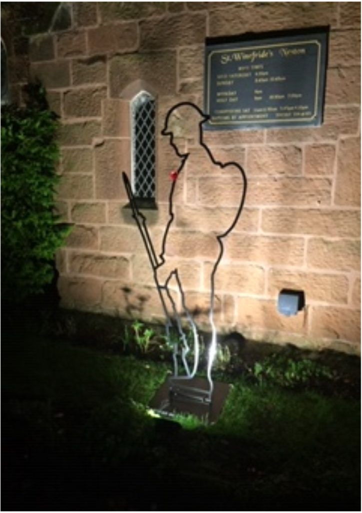 WWI Commemorative Tommy Silhouette outside St Winefride's Church - evening photograph with silhouette illuminated by outdoor lights.